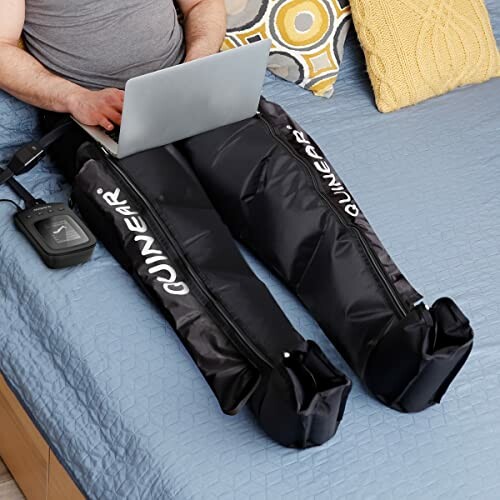 Person using leg compression massage device on bed.